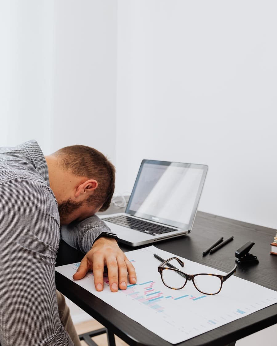 Homme épuisé, la tête posée sur son bureau, à côté de son ordinateur portable